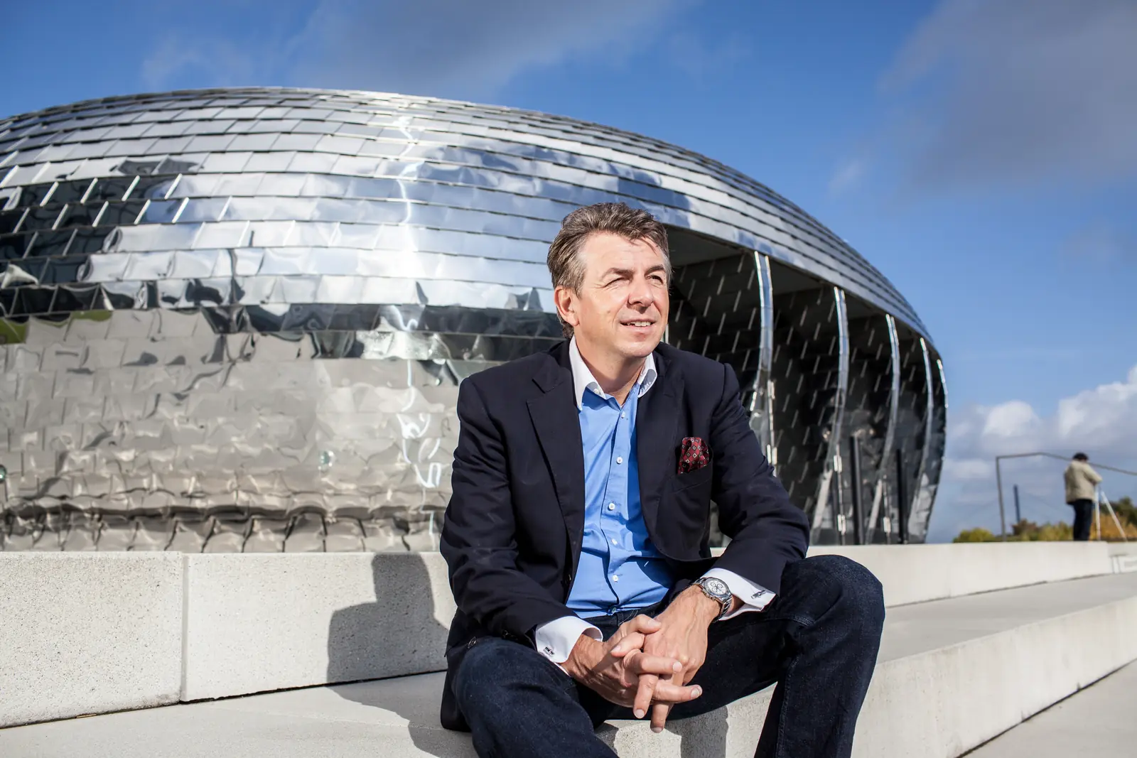Motivationstrainer Dirk Schmidt sitzend vor einem verspiegelten Kuppelbau